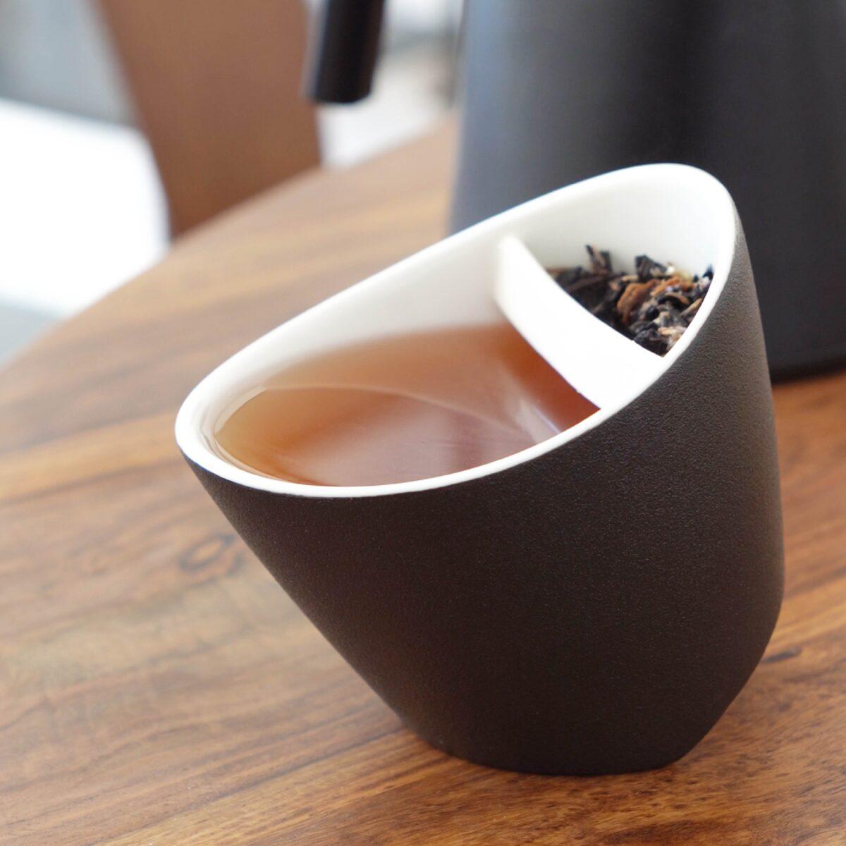 Black tilting teacup filled with pu erh orange tea